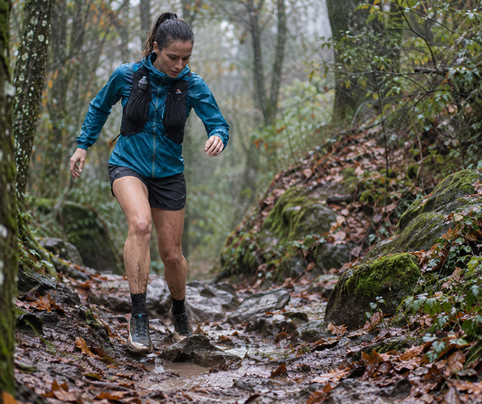 Trailrunner die in de regen een modderig pad oversteekt